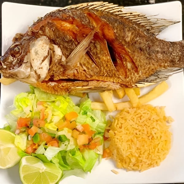 Fried whole fish with rice, french fries, salad, pico de gallo, and lime wedges.