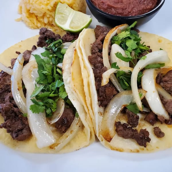 Two El Sol Restaurant carne asada tacos with onions and cilantro, served with rice and beans.