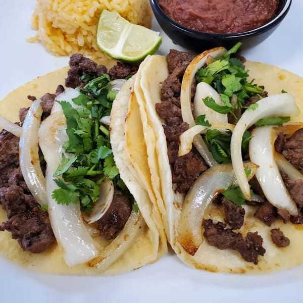 Two El Sol Restaurant Mexican tacos with steak, onions, cilantro, rice, and salsa.