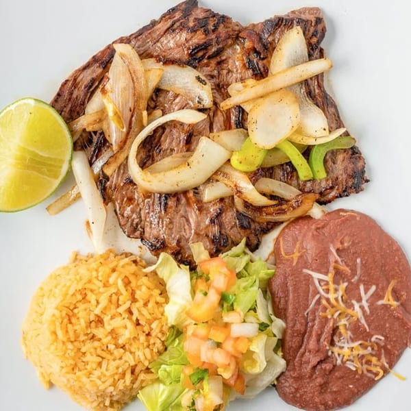 Grilled steak with onions and peppers, served with rice, refried beans, and a side salad.