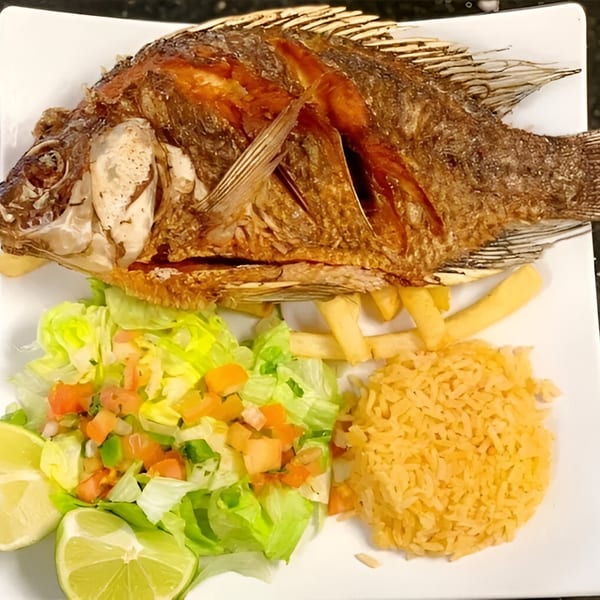 Whole fried tilapia with rice, french fries, and a fresh salad with lime wedges.