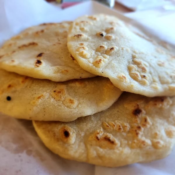 Close-up of several warm, fluffy Mexican tortillas with light brown spots, stacked on white paper.