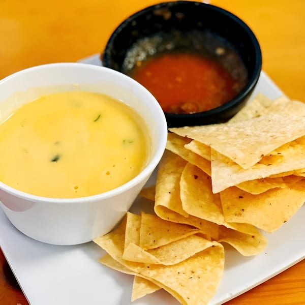 A white bowl of queso dip, a black bowl of salsa, and a pile of tortilla chips.