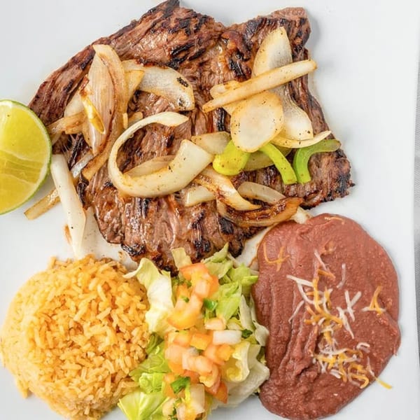 Grilled steak with sautéed onions and peppers, served with rice, refried beans, and a side salad.